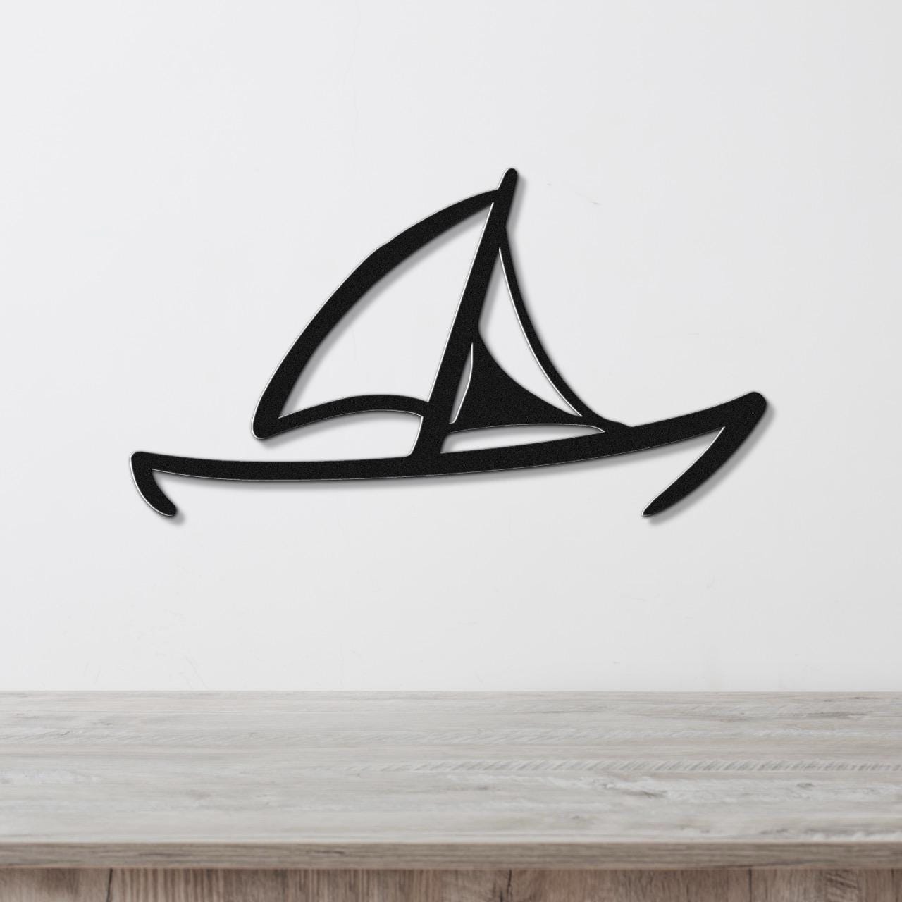 Black metal sailboat wall art with a silhouette design and internal cutouts, mounted on a white wall above a light wood surface.