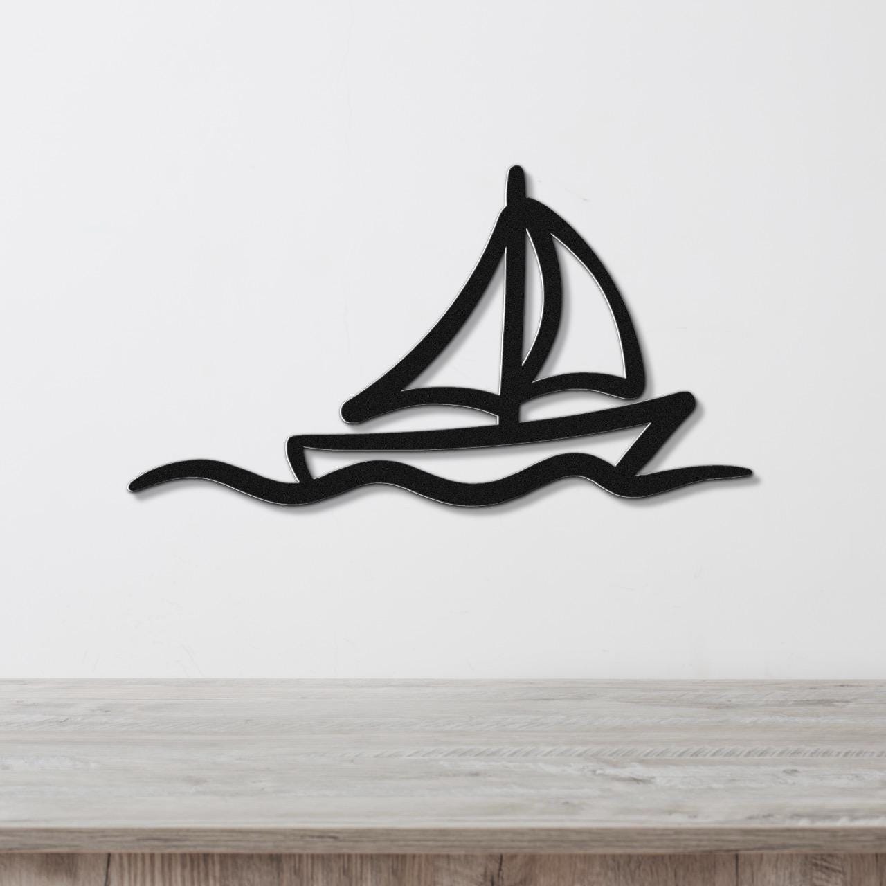 Black metal sailboat wall art with wave cutout, mounted on a white wall above a light wood counter.