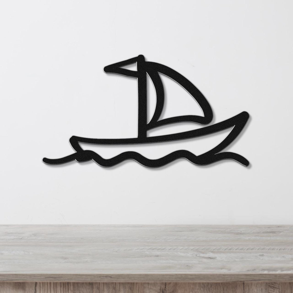 Black metal sailboat wall art with wave cutouts, mounted on a white wall above a light wood surface.