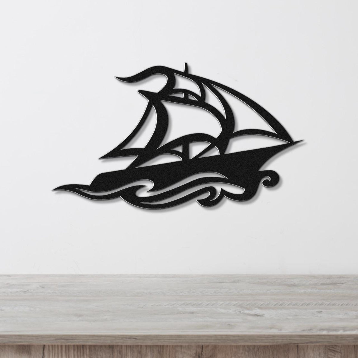Black metal sailboat wall art with wave cutouts, mounted on a white wall above a wooden surface.