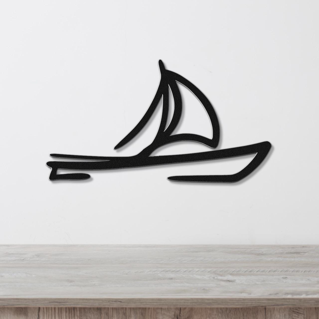 Black metal sailboat wall art with a silhouette design, mounted on a white wall above a wooden surface.