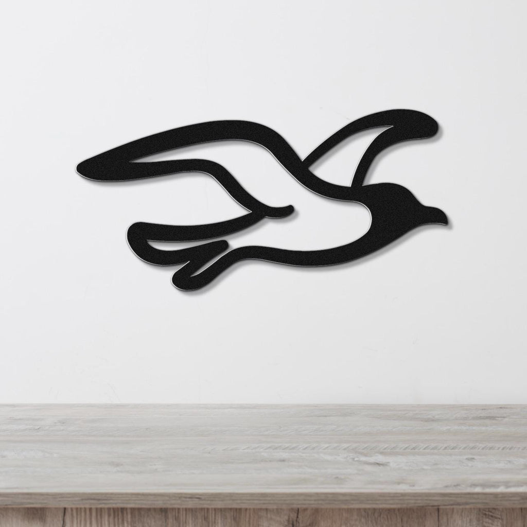 Black metal seagull wall art with flowing wing cutouts, mounted on a white wall above a light wood surface.