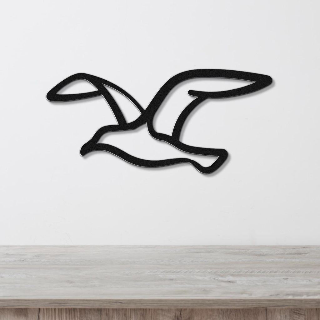 Black metal seagull wall art with wing cutouts, mounted on a white wall above a light wood counter.