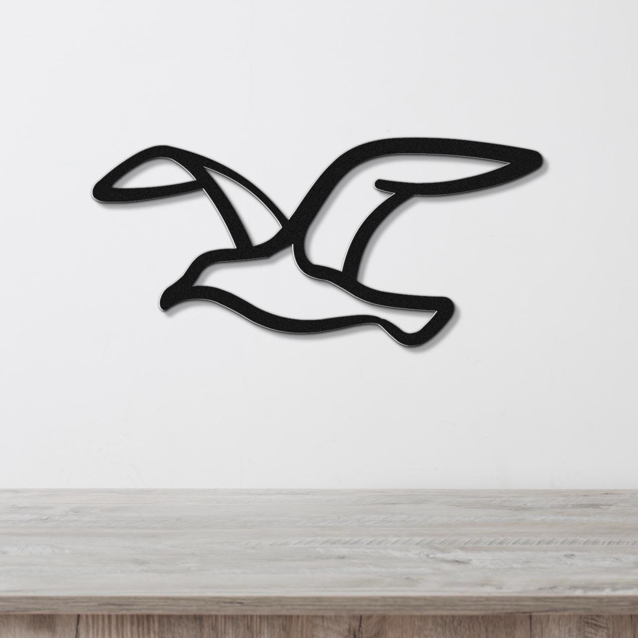 Black metal seagull wall art with wing cutouts, mounted on a white wall above a light wood counter.