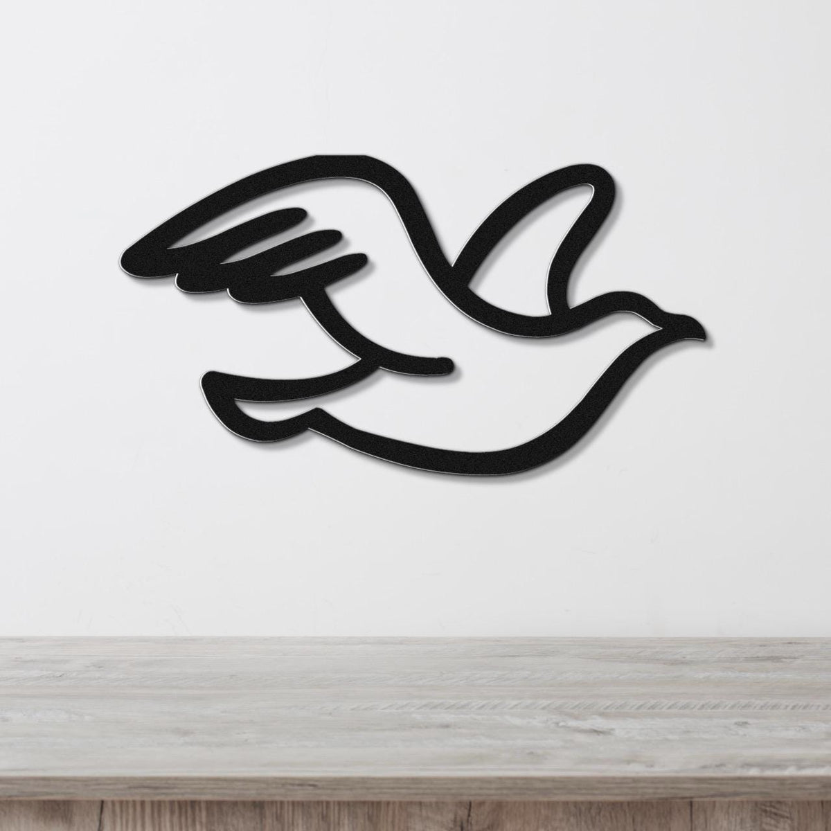 Black metal seagull wall art with a cutout silhouette design, mounted on a white wall above a light wood surface.
