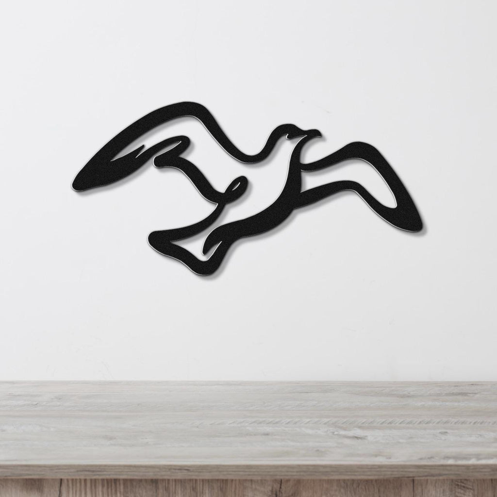 Black metal seagull wall art with flowing wing cutouts, mounted on a white wall above a light wood surface.