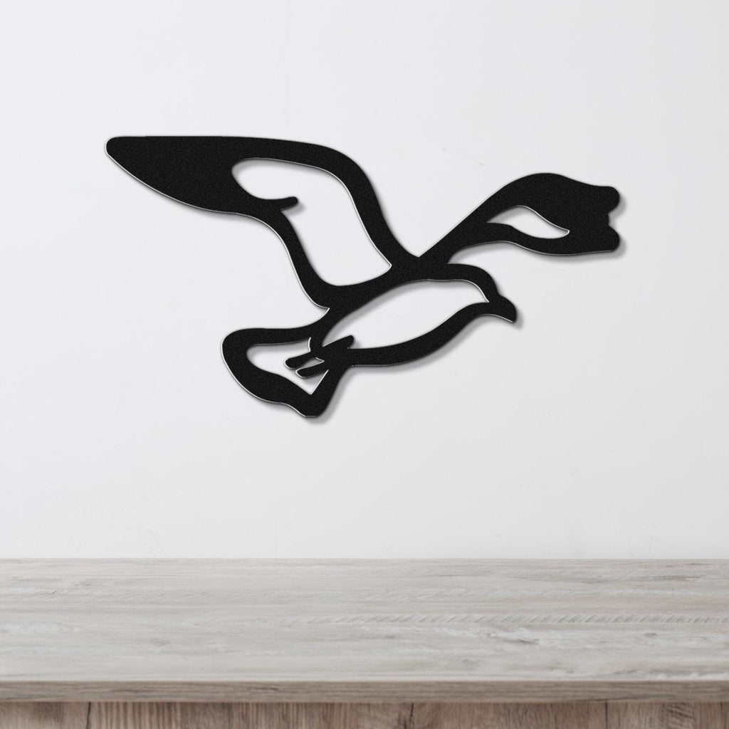 Black metal seagull wall art with wing and tail cutouts, mounted on a white wall above a light wood surface.