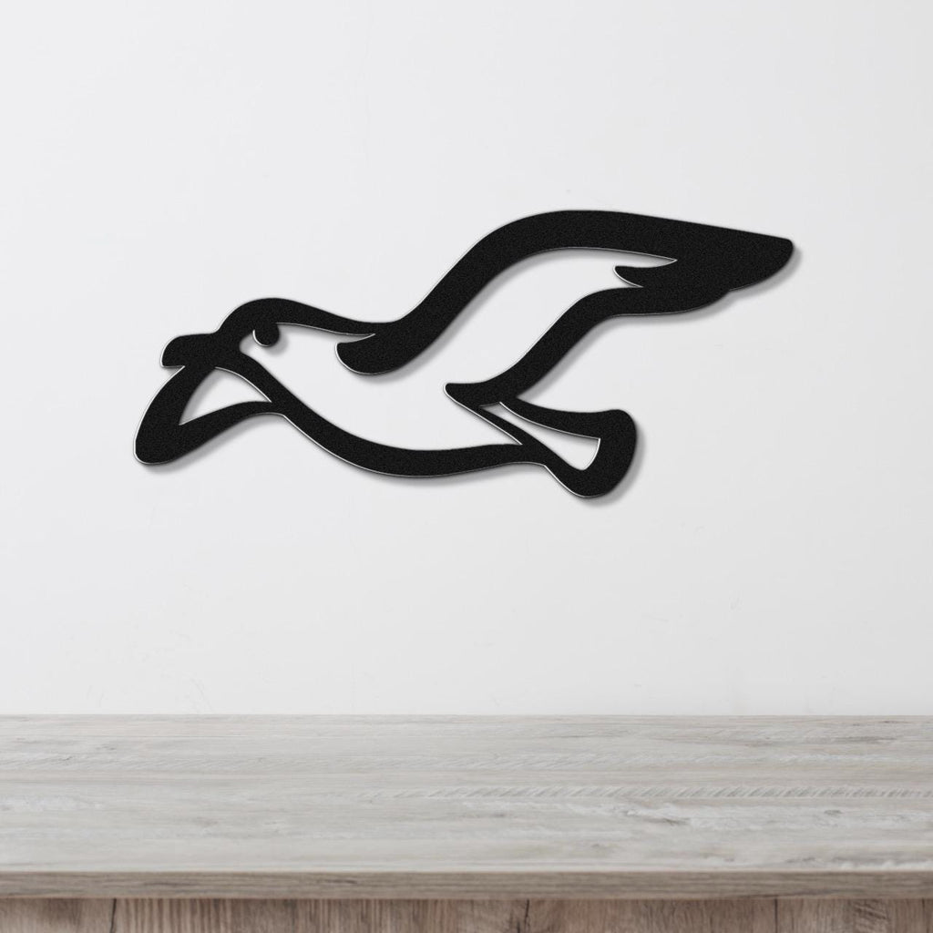 Black metal seagull wall art with a sleek silhouette design, mounted on a white wall above a light wood surface.