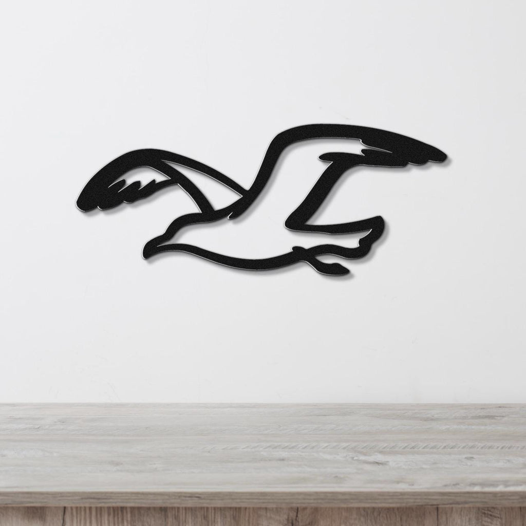 Black metal seagull wall art with a cutout silhouette design, mounted on a white wall above a light wood surface.