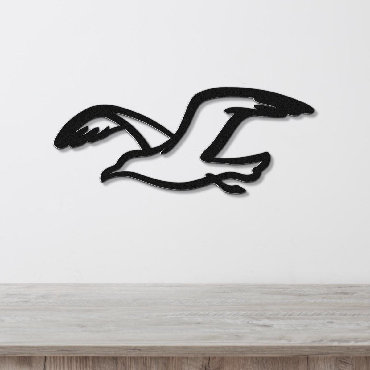 Black metal seagull wall art with a cutout silhouette design, mounted on a white wall above a light wood surface.