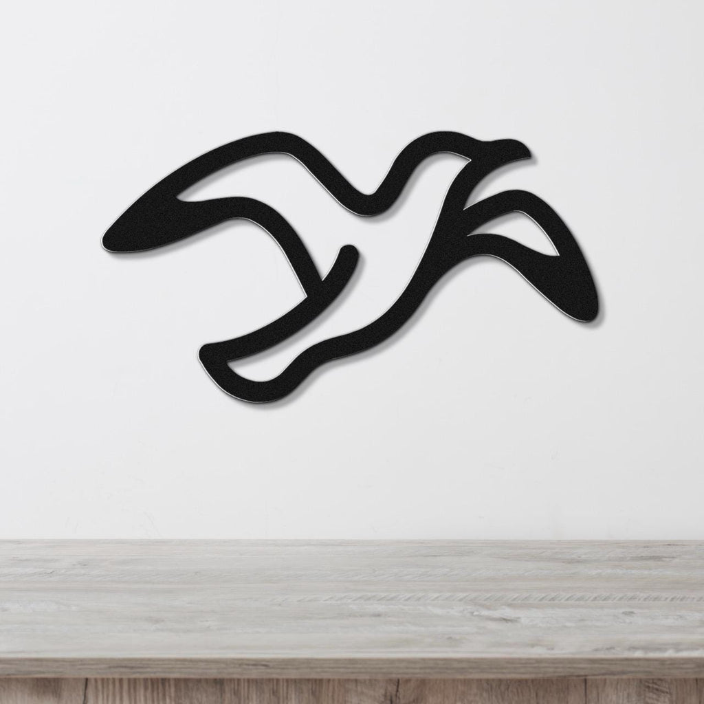 Black metal seagull wall art with flowing motion lines, mounted on a white wall above a light wood surface.