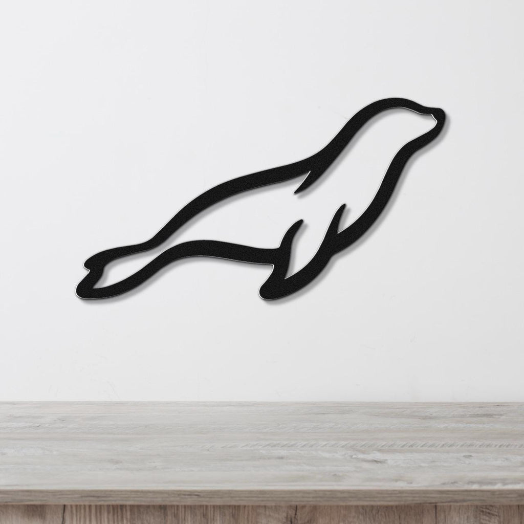 Black metal sea lion wall art with a sleek silhouette design, mounted on a white wall above a light wood surface.