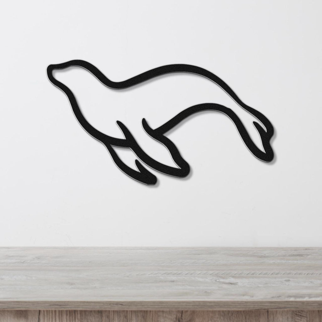 Black metal sea lion wall art with a sleek silhouette design, mounted on a white wall above a light wood surface.