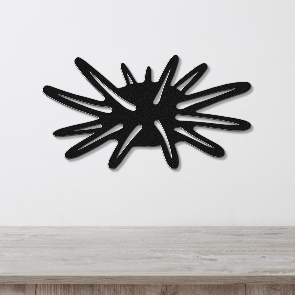 Black metal wall art cutout in a sea urchin shape with radiating spines, mounted on a white wall above a light wood surface.