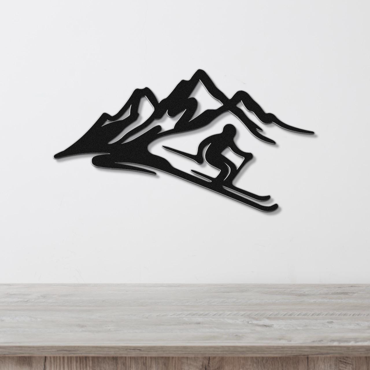Black metal wall sculpture of a skier in motion against mountain peaks, mounted on a white wall above a wooden surface.