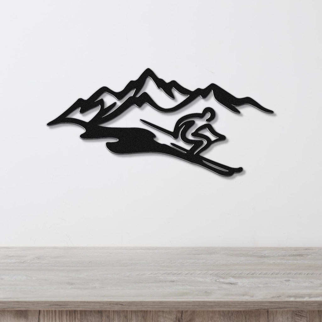 Black metal wall art featuring a skier silhouette in motion against a mountain range, mounted on a white wall above a wooden surface.