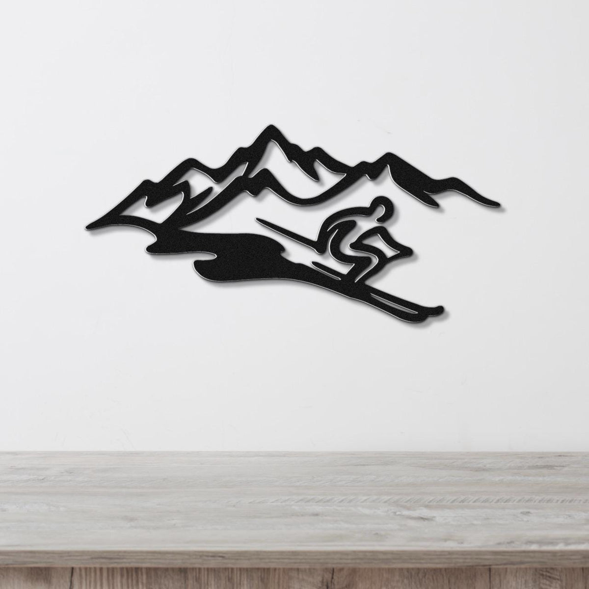 Black metal wall art featuring a skier silhouette in motion against a mountain range, mounted on a white wall above a wooden surface.