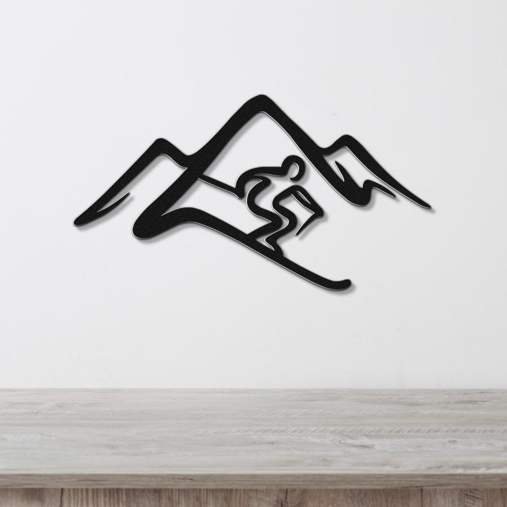 Black metal wall art featuring a skier silhouette cutout within a mountain range, mounted on a white wall above a wooden surface.