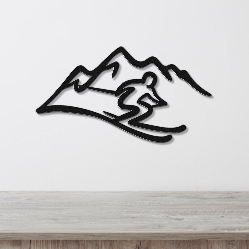 Black metal wall art featuring a skier silhouette in motion against a mountain range, mounted on a white wall above a wooden surface.
