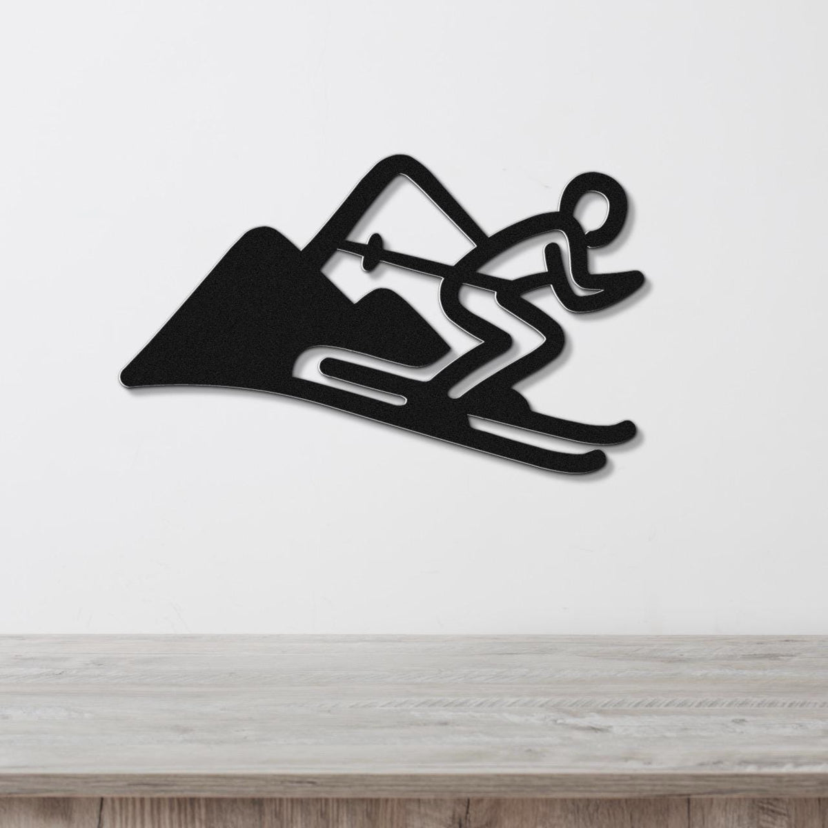 Black metal wall art featuring a skier silhouette in motion with mountain cutout, mounted on a white wall above a wooden surface.