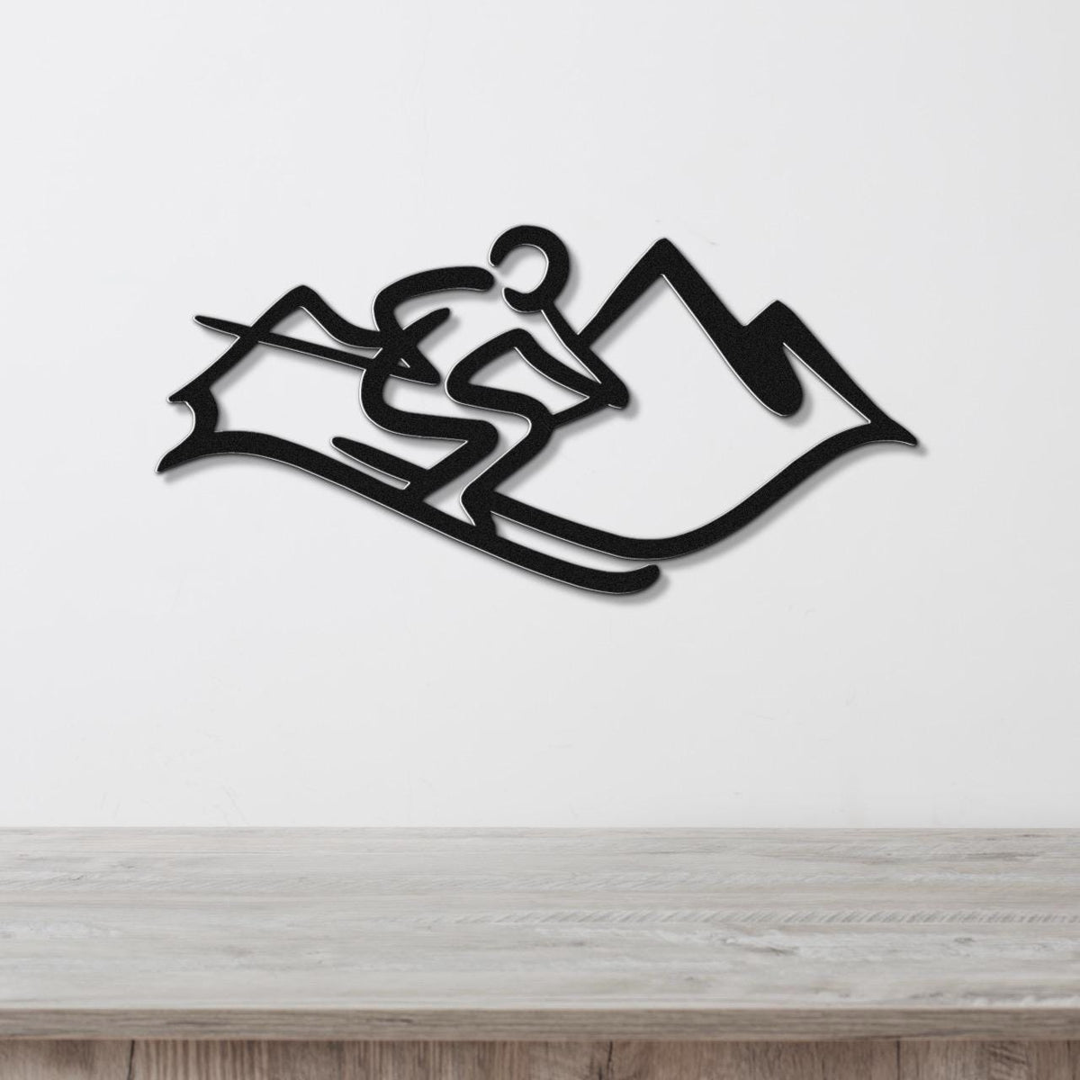 Black metal wall art featuring a skier silhouette and mountain cutout, mounted on a white wall above a light wood surface.