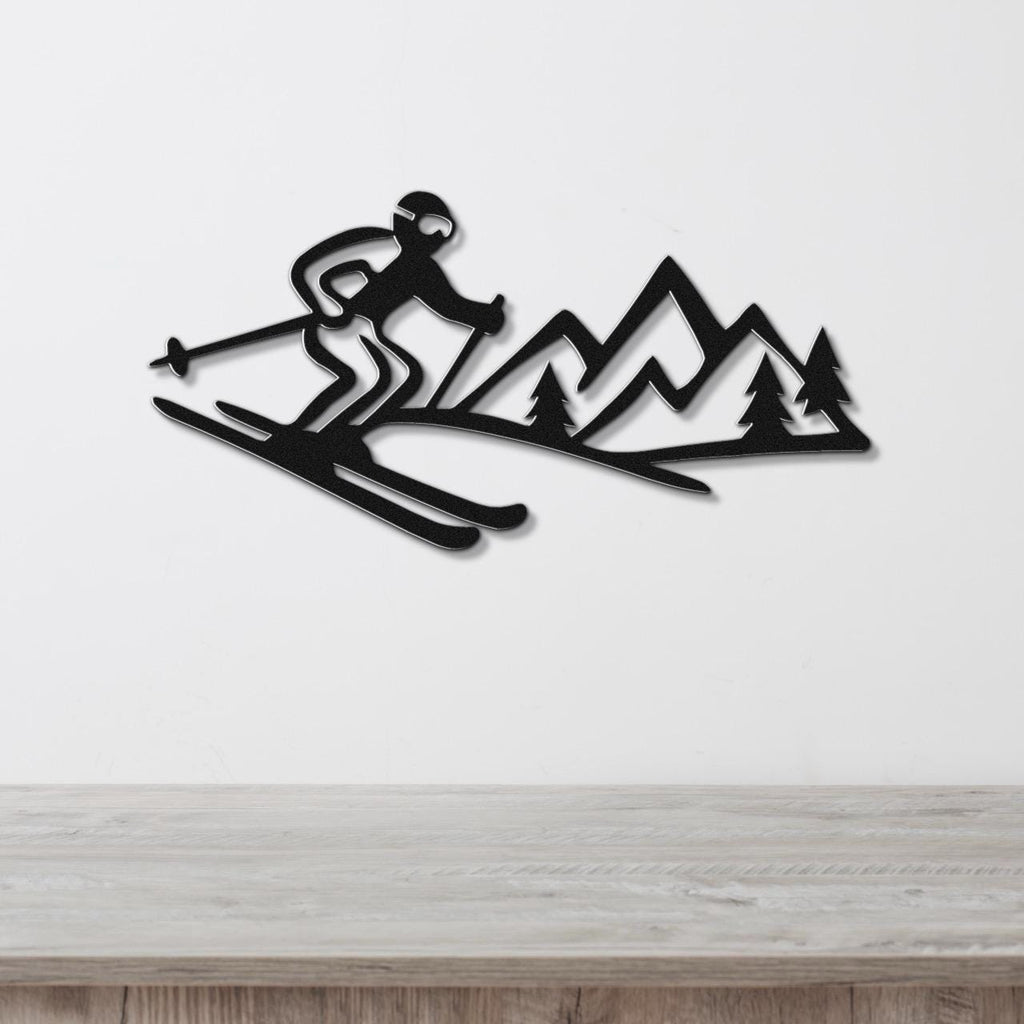 Black metal wall art cutout of a skier in motion with mountain and tree silhouettes, mounted on a white wall above a wooden surface.