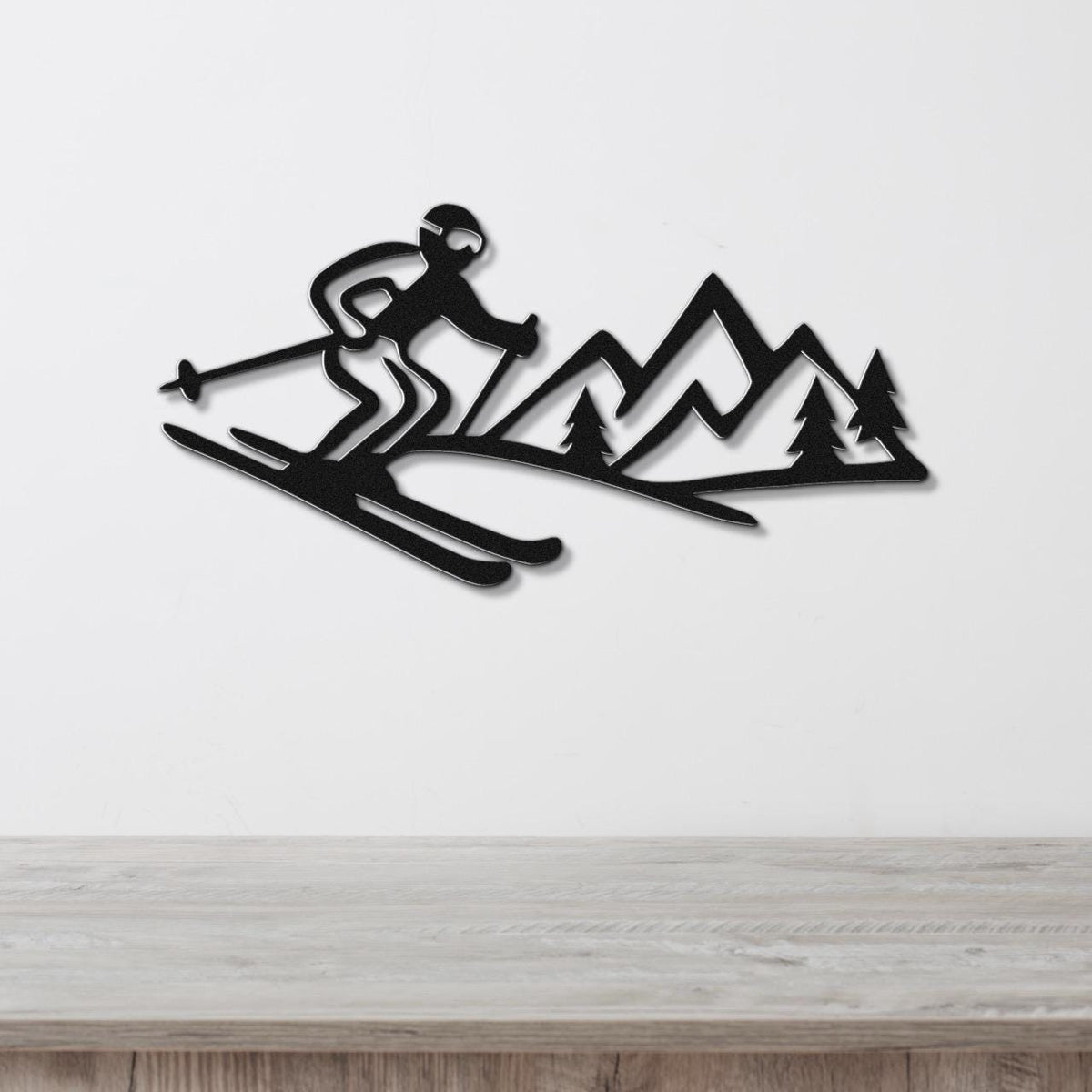 Black metal wall art cutout of a skier in motion with mountain and tree silhouettes, mounted on a white wall above a wooden surface.