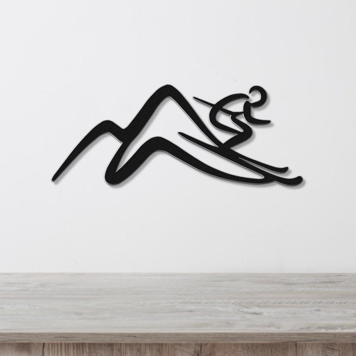 Black metal wall art featuring a skier silhouette gliding over mountain peaks, mounted on a white wall above a light wood counter.