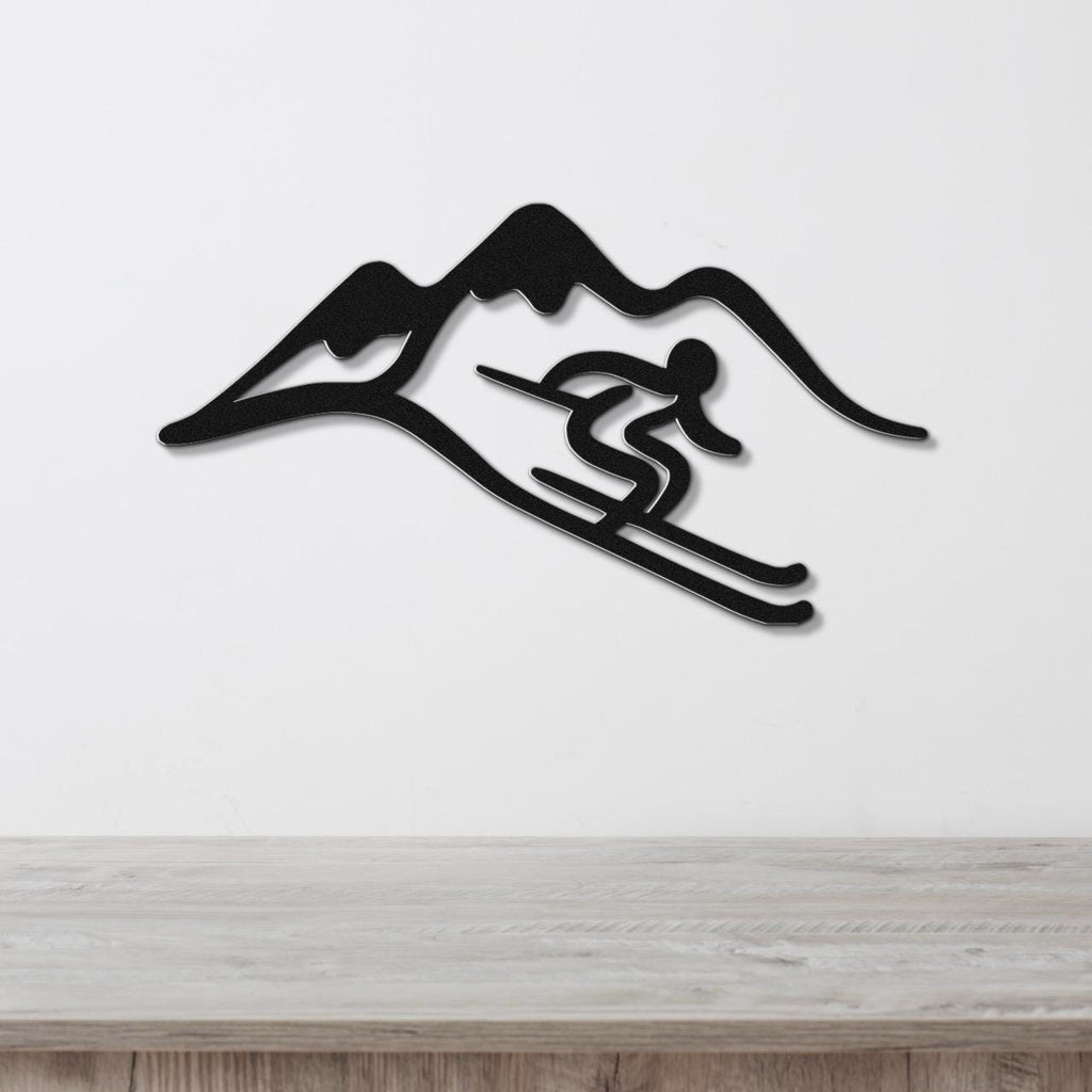 Black metal wall art featuring a skier silhouette in motion against a mountain range, mounted on a white wall above a light wood surface.