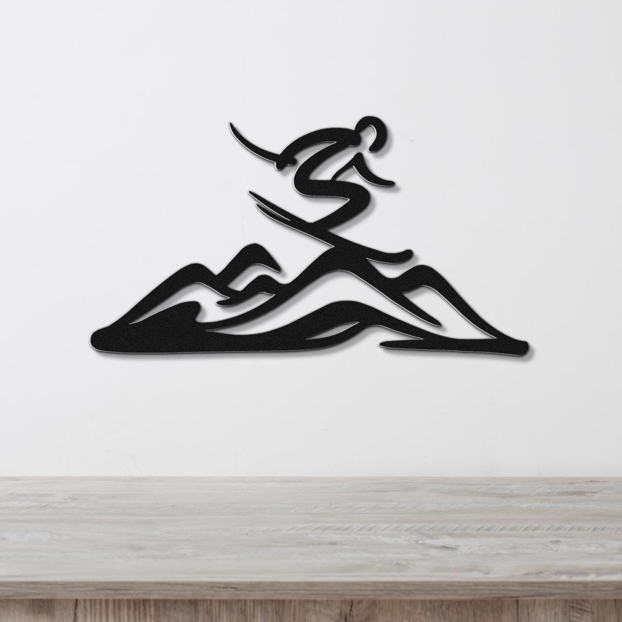Black metal wall art featuring a skier silhouette above layered mountain cutouts, mounted on a white wall above a light wood counter.
