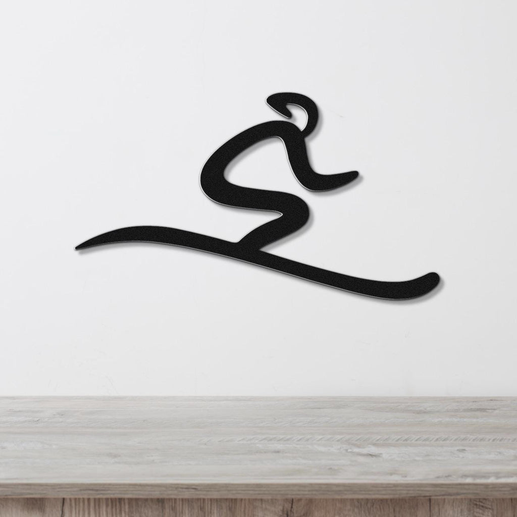 Black metal wall art in a dynamic skiing silhouette, mounted on a white wall above a light wood surface.