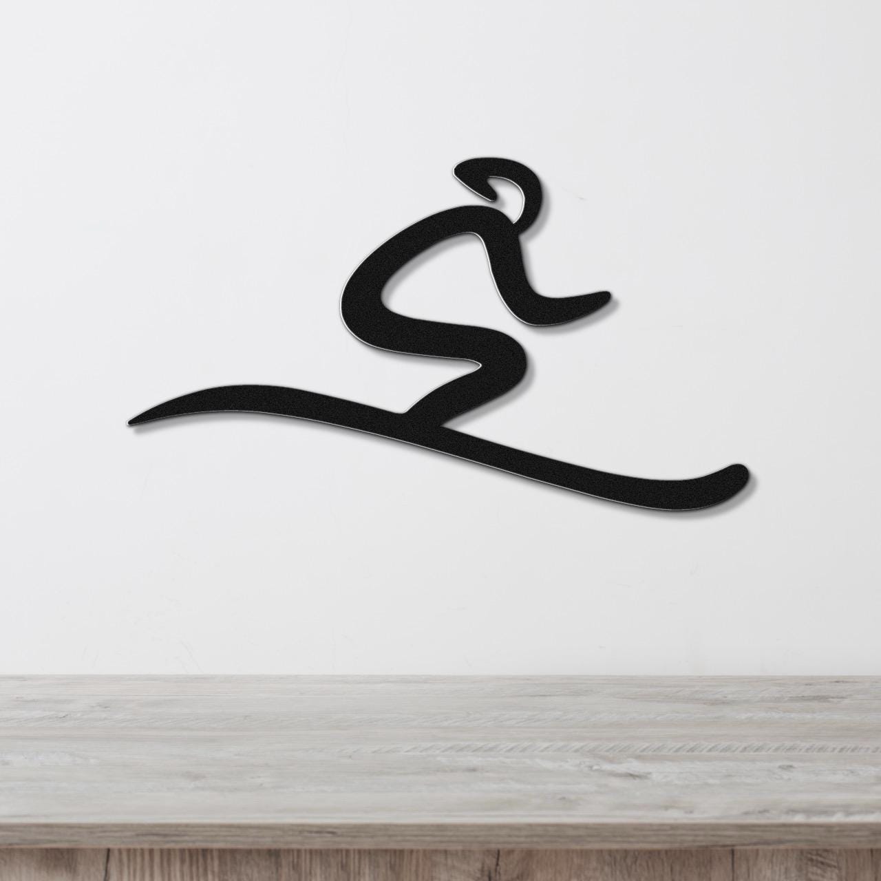 Black metal wall art in a dynamic skiing silhouette, mounted on a white wall above a light wood surface.