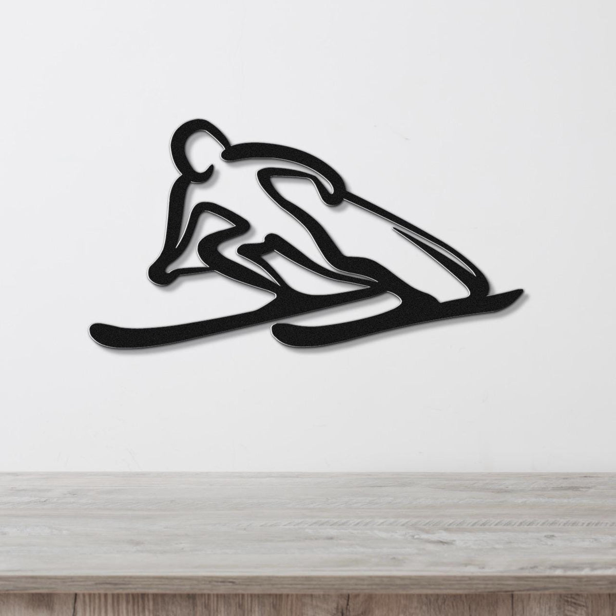 Black metal wall art of a skier silhouette with motion-line cutouts, mounted on a white wall above a light wood counter.