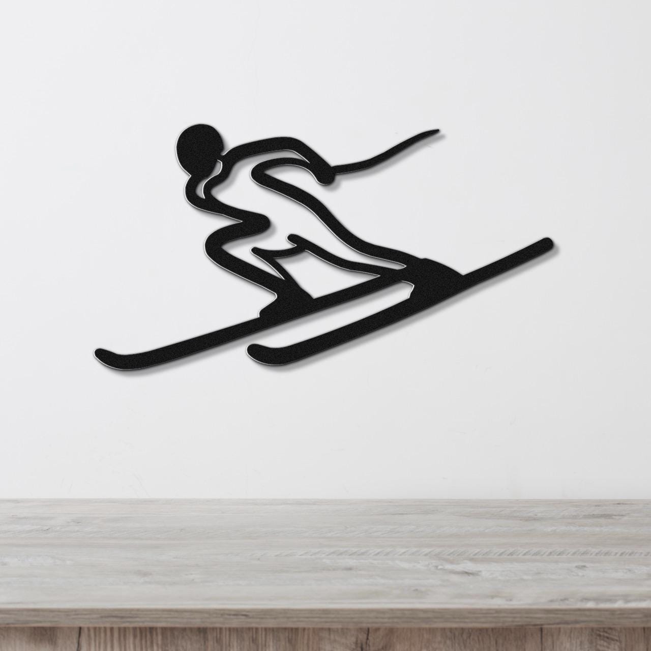 Black metal wall art of a skier silhouette with dynamic motion lines, mounted on a white wall above a light wood surface.