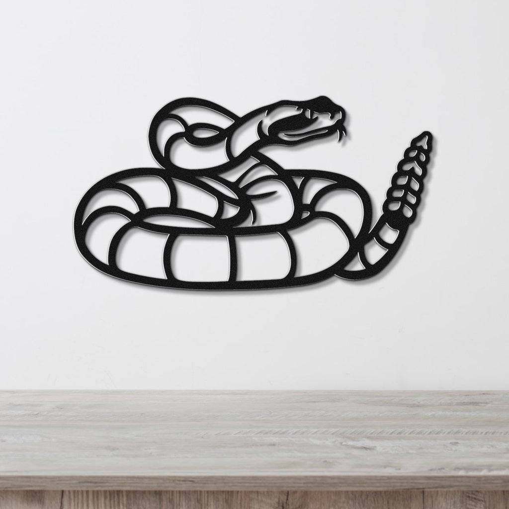 Black metal snake wall art with coiled body and raised head, featuring internal cutout details, mounted on a white wall above a wooden surface.
