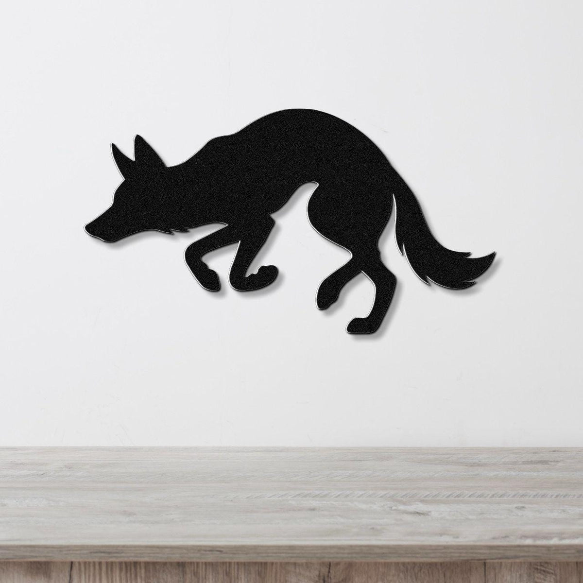 Black metal coyote wall art in a crouching silhouette, mounted on a white wall above a light wood surface.