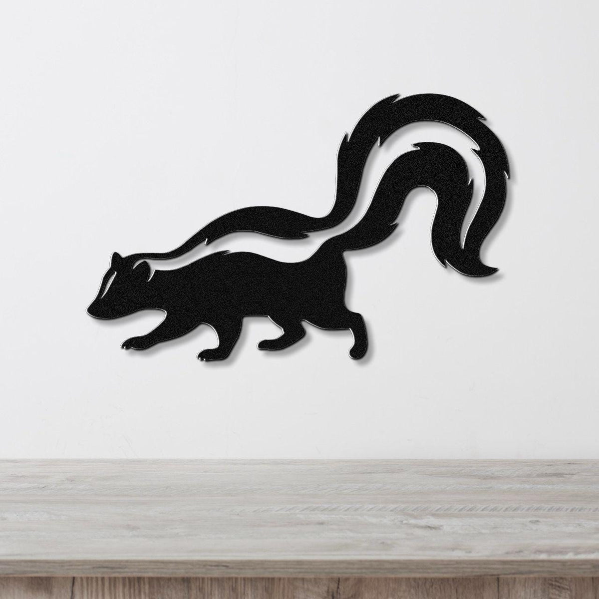 Black metal skunk wall art with a white stripe cutout, mounted on a white wall above a wooden surface.