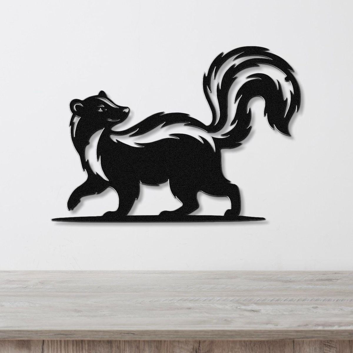 Black metal skunk wall art silhouette with a raised tail and white stripe, mounted on a white wall above a wooden surface.