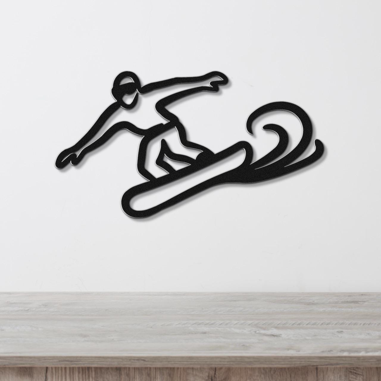 Black metal wall art of a snowboarder in motion, featuring a silhouette cutout with dynamic lines, mounted on a white wall above a wooden surface.
