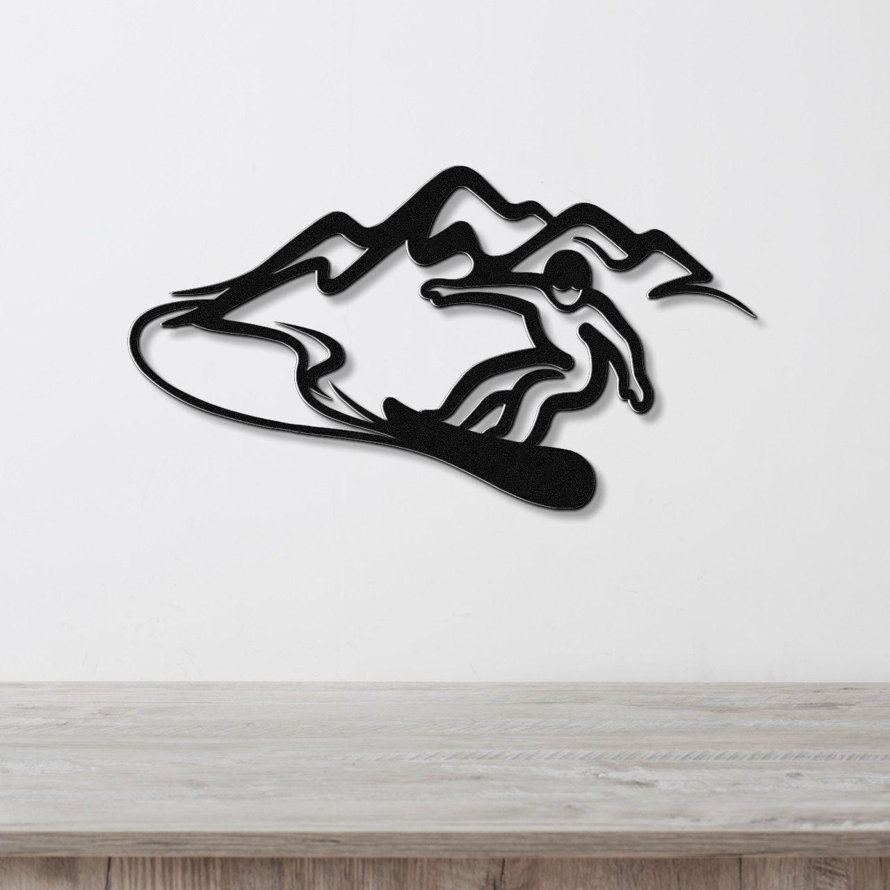Black metal wall art featuring a silhouette of a snowboarder in motion against mountain peaks, mounted on a white wall above a wooden surface.