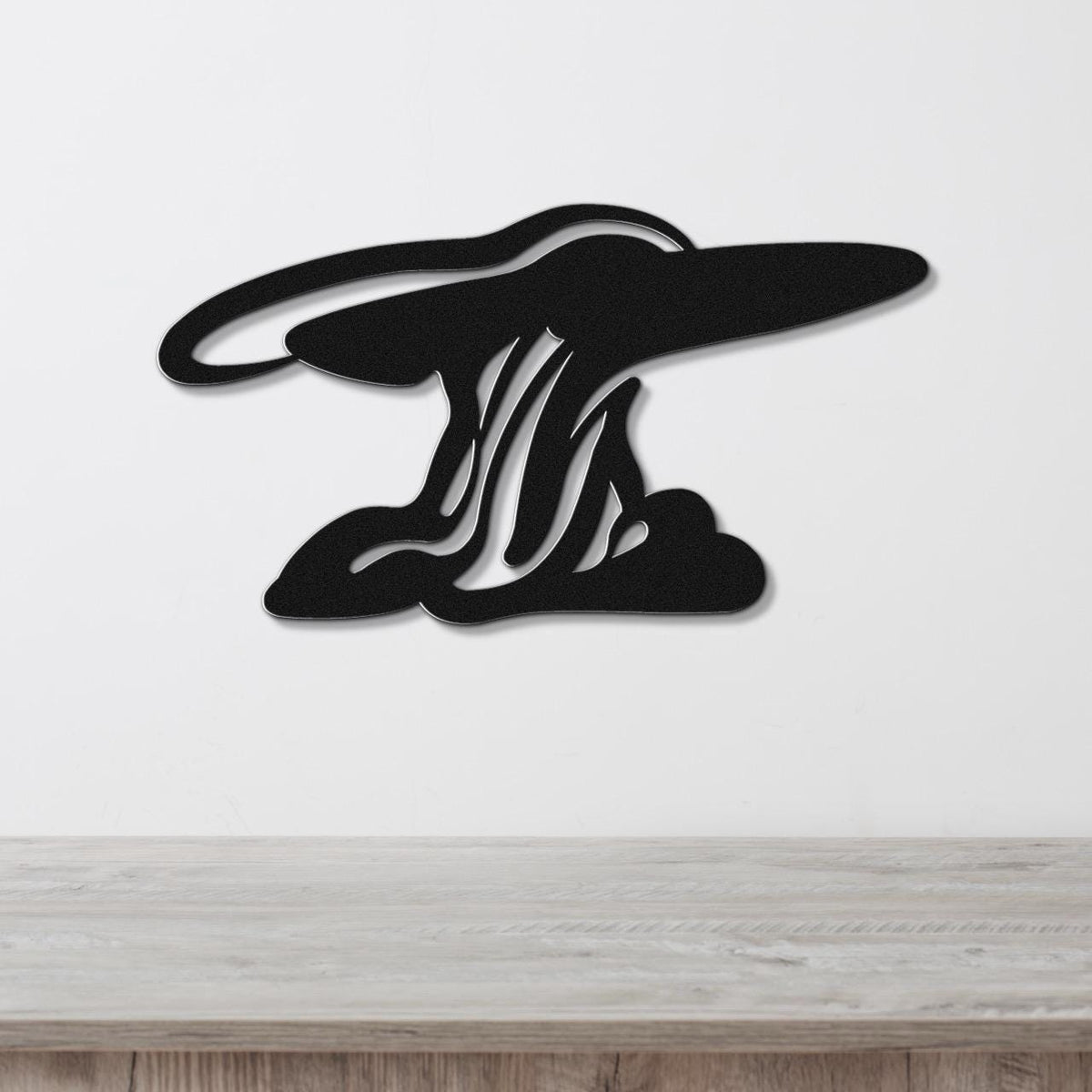 Black metal wall art silhouette of storm clouds with internal cutout lines, mounted on a white wall above a light wood surface.