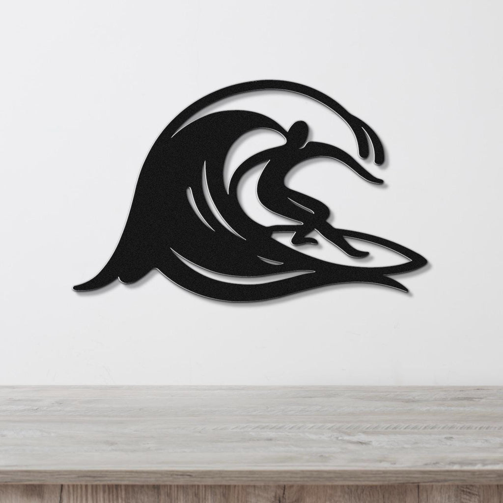 Black metal wall art featuring a surfer silhouette riding a flowing wave, mounted on a white wall above a wooden surface.
