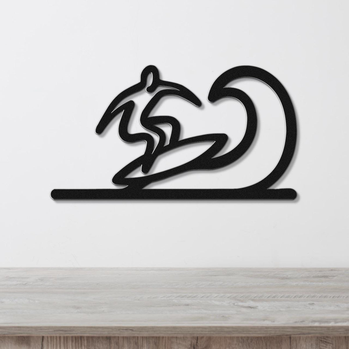 Black metal wall art featuring a surfer silhouette riding a wave, mounted on a white wall above a wooden surface.