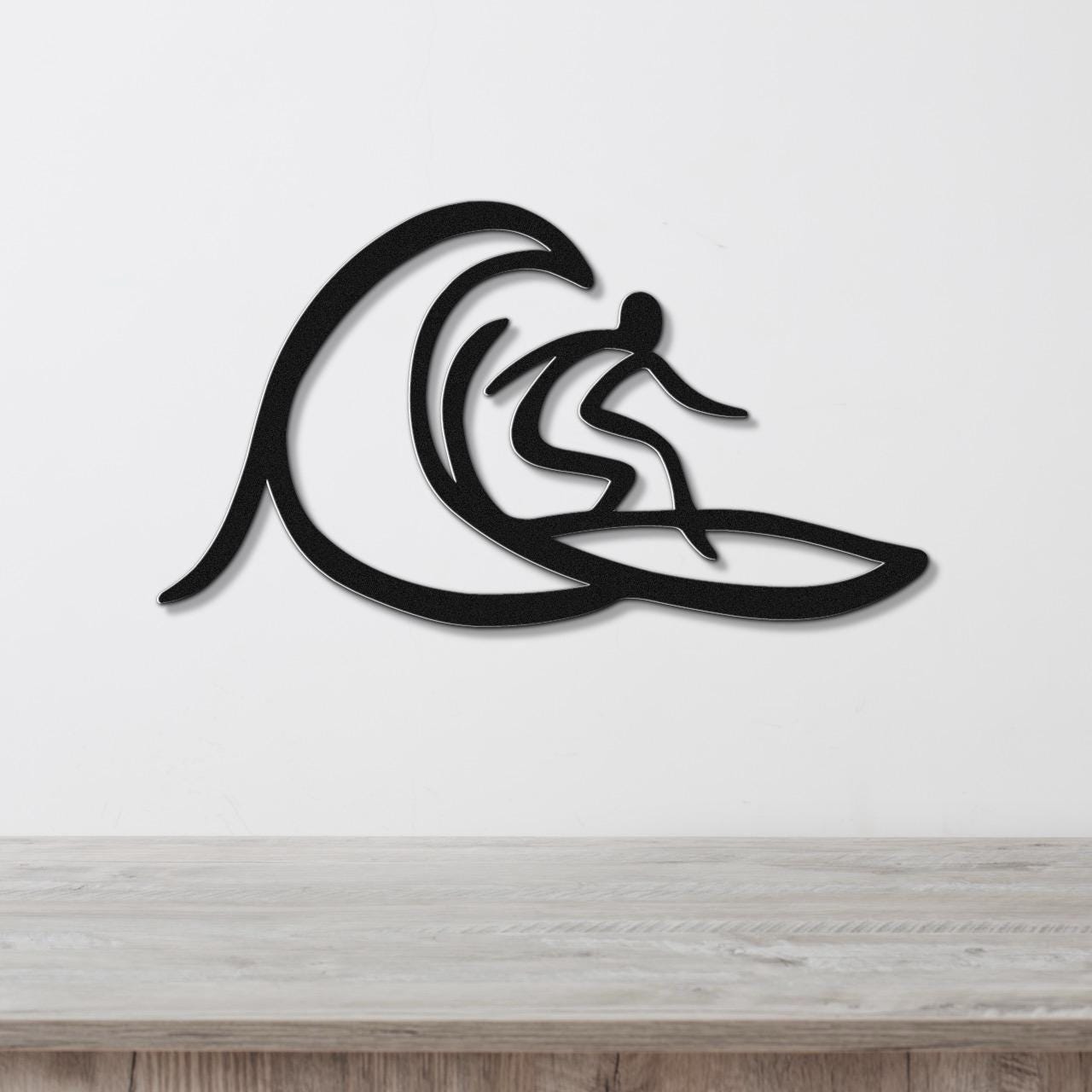 Black metal wall art featuring a surfer silhouette riding a wave, mounted on a white wall above a wooden surface.