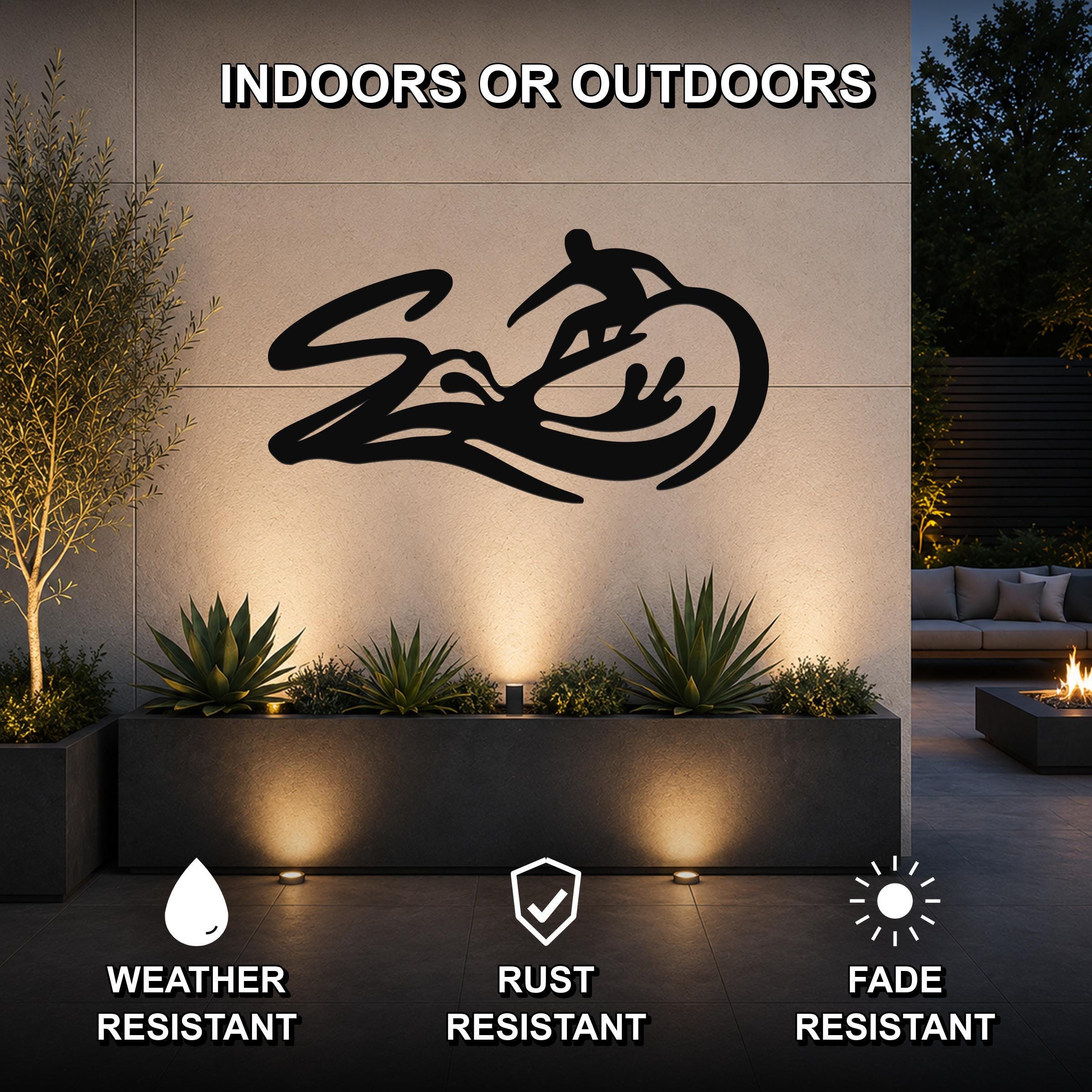 Black metal surfer wall art with wave and rider silhouette, mounted on an outdoor wall above a planter in a modern patio setting.