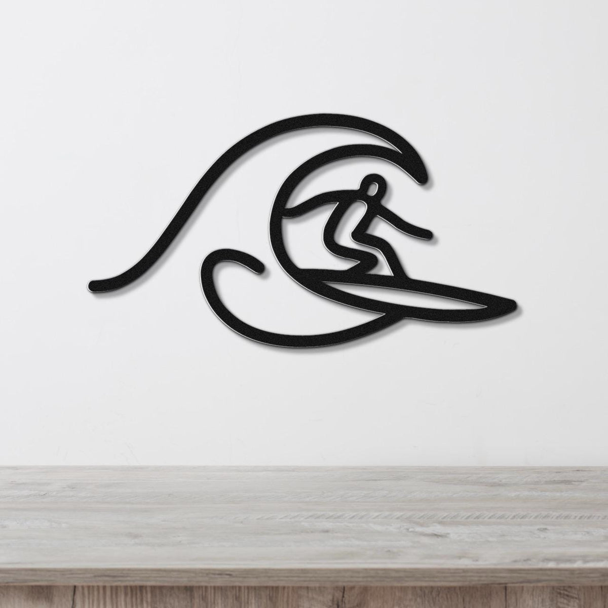 Black metal wall art featuring a surfer silhouette riding a wave, mounted on a white wall above a wooden surface.