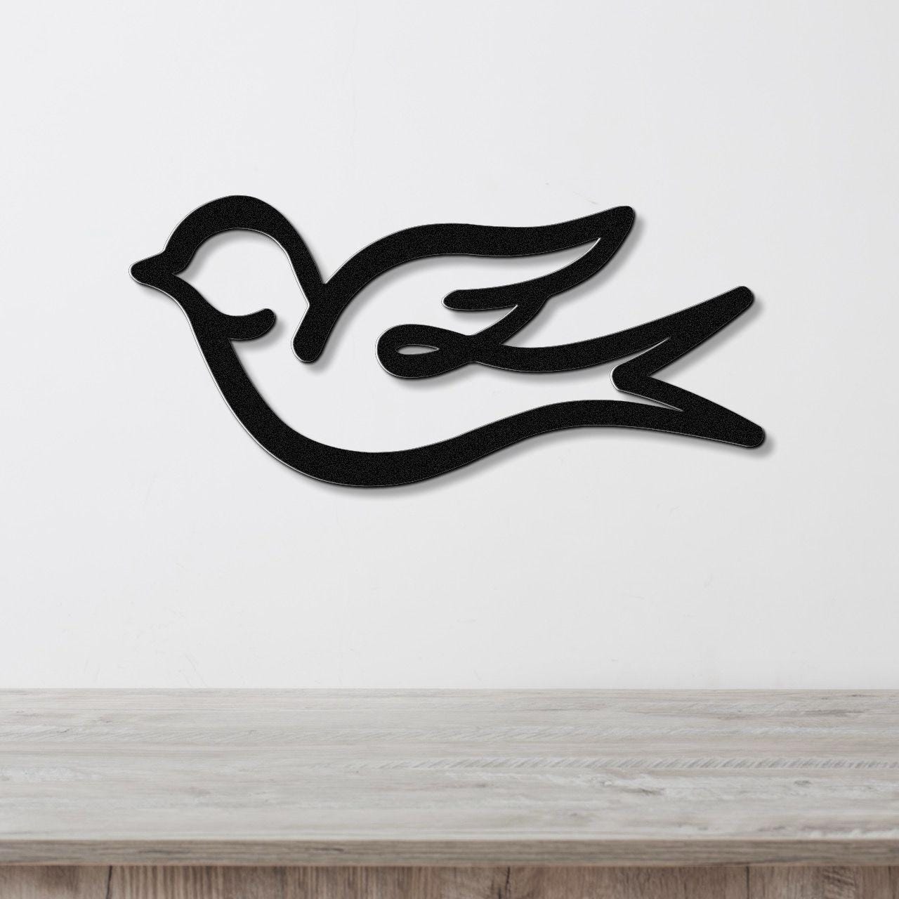 Black metal swallow bird wall art with flowing silhouette design, mounted on a white wall above a light wood surface.