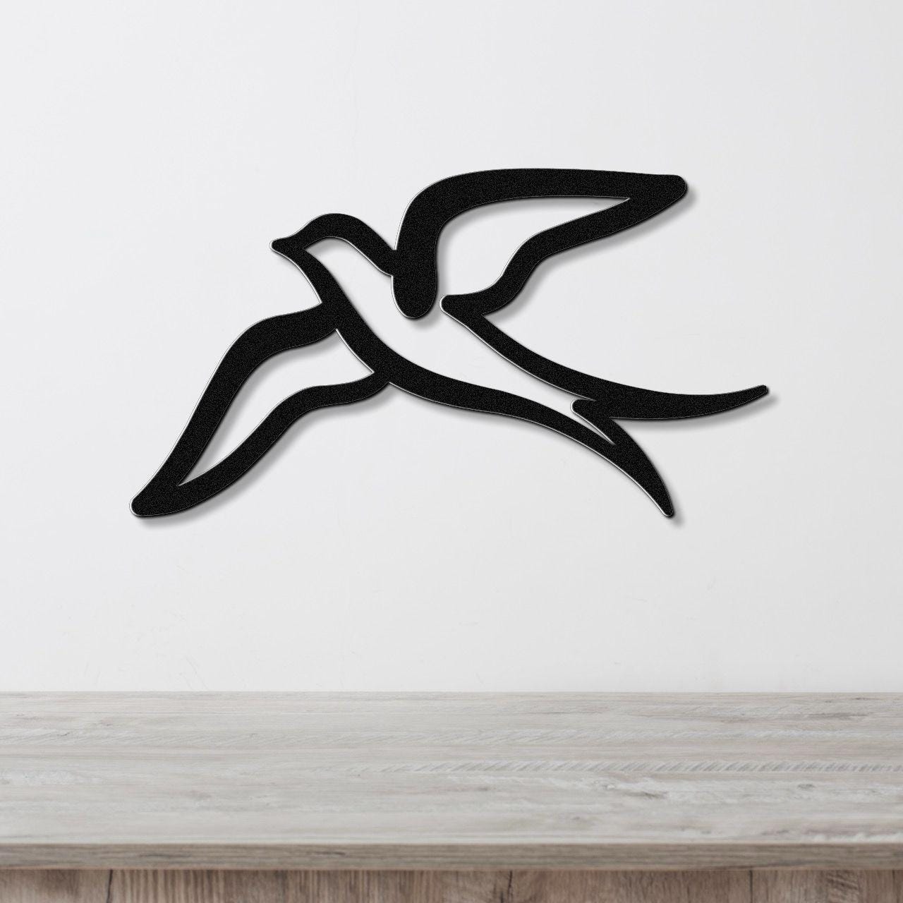 Black metal swallow bird wall art with a graceful silhouette and open-wing cutout, mounted on a white wall above a light wood counter.