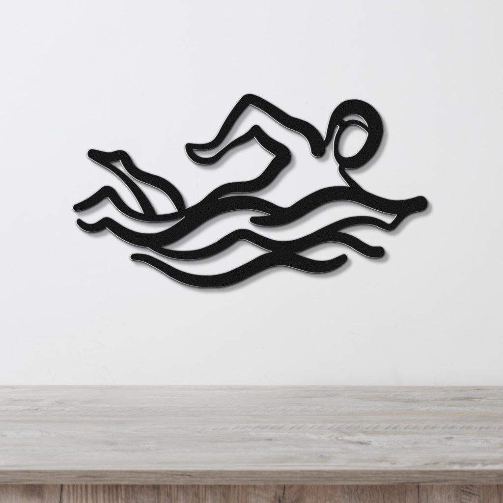 Black metal wall art depicting a swimmer in motion with wavy water lines, mounted on a white wall above a wooden surface.