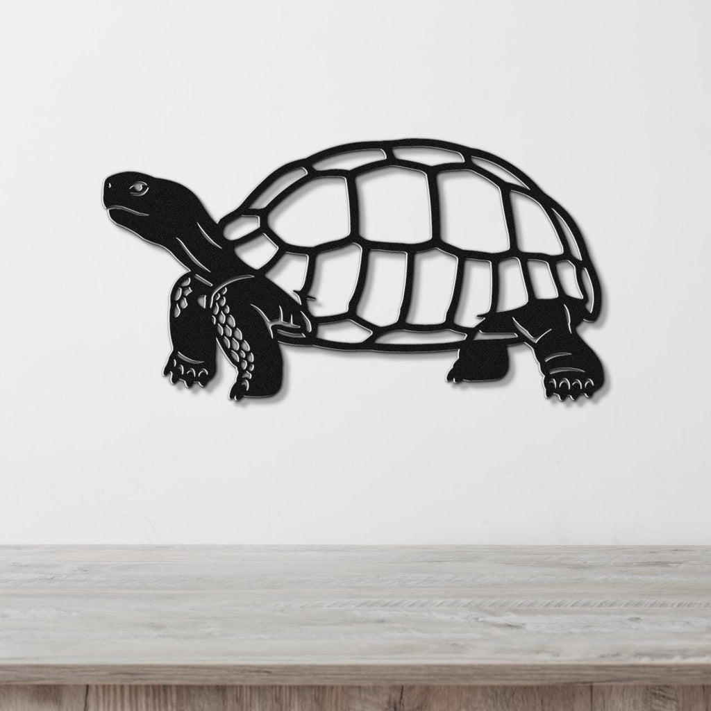 Black metal tortoise wall art with a cutout shell and detailed legs, mounted on a white wall above a wooden surface.